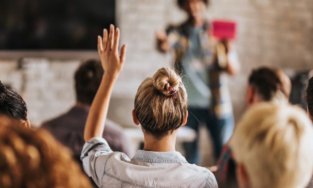 A woman raising her hand to ask a question in a meeting.